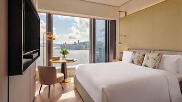 A hotel room with a large bed, a TV, a small table with a plant, and a view of a cityscape.