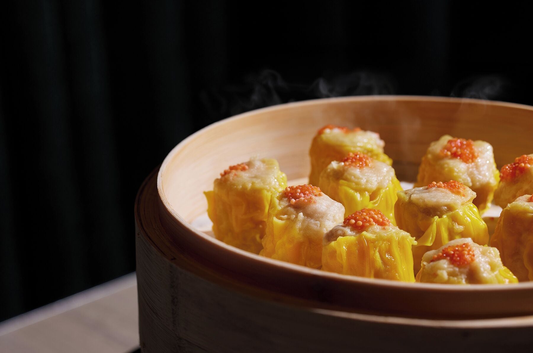 Una vaporera de bambú con dumplings cubiertos de huevas.