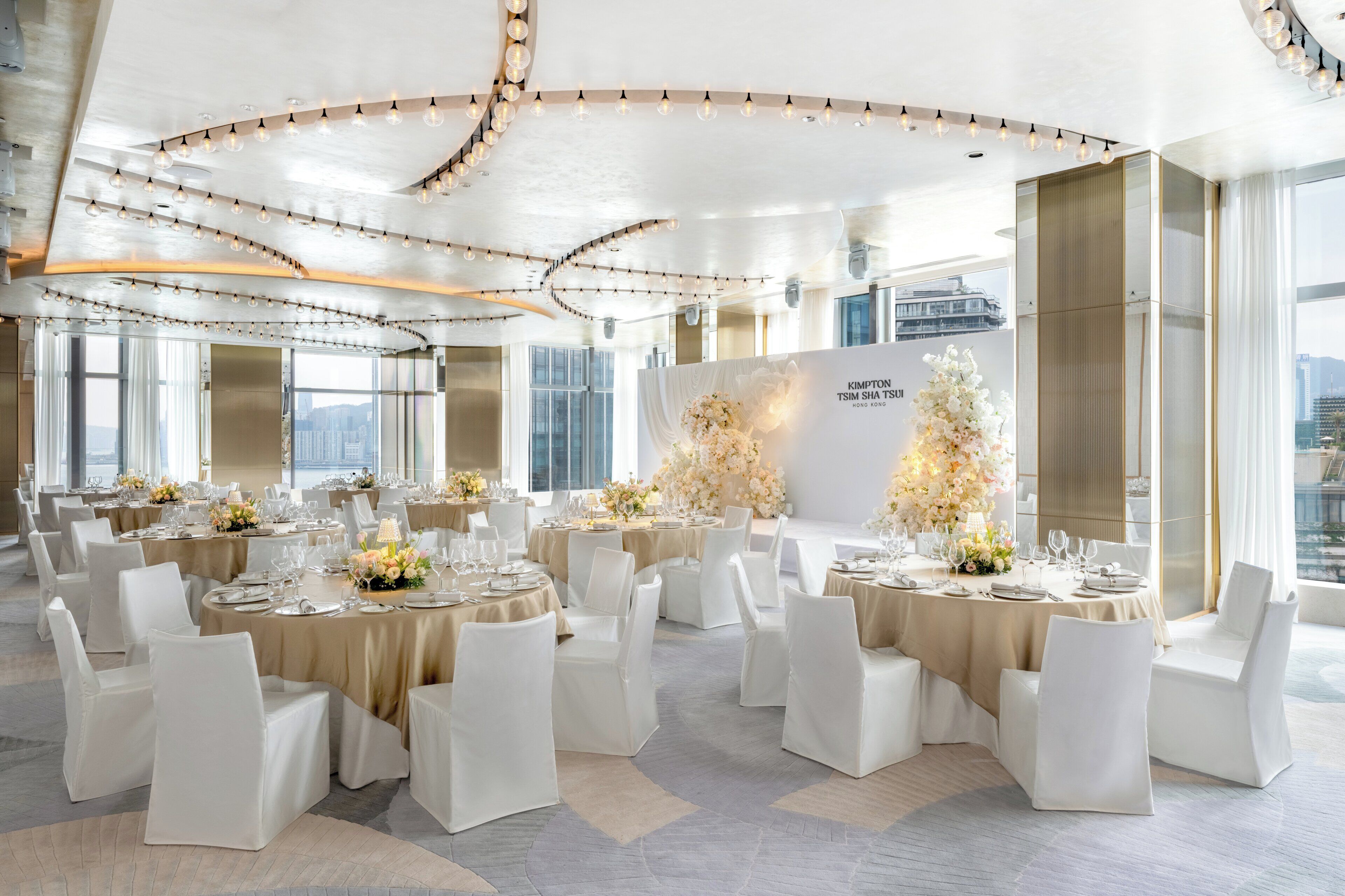 A spacious banquet hall with round tables, white chairs, and floral centerpieces.