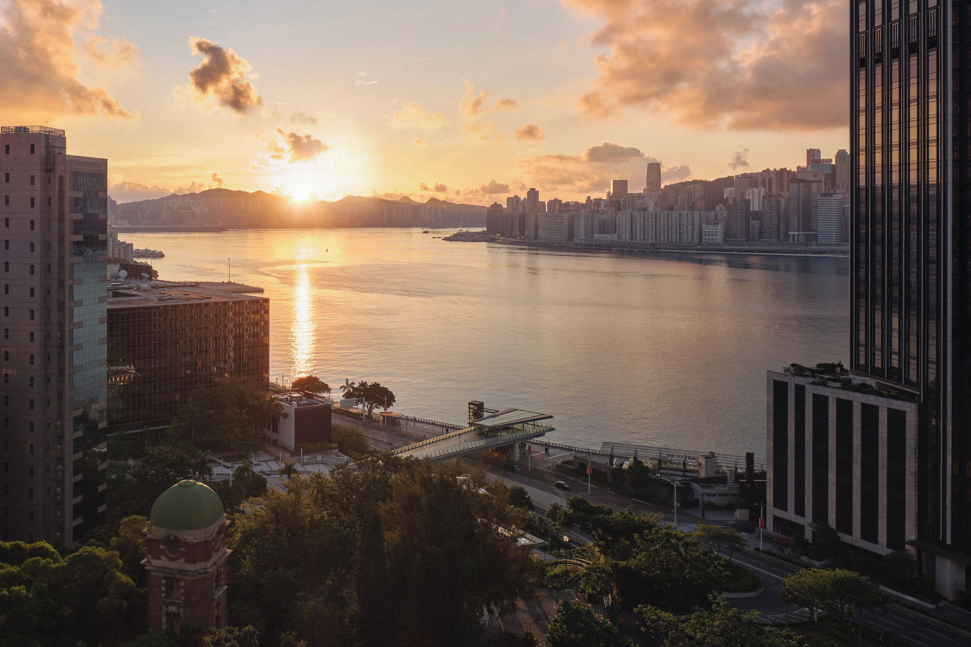A cityscape with a river, modern buildings, and a bridge during sunset.