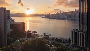 A cityscape with a river, modern buildings, and a bridge during sunset.