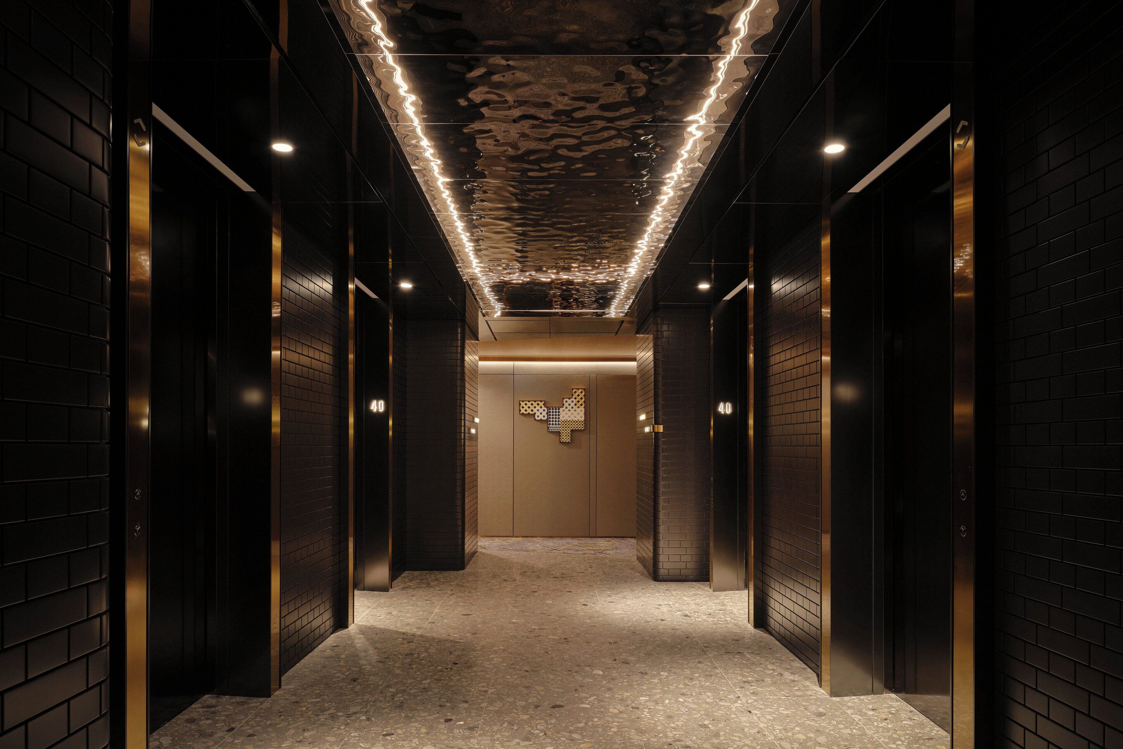 A corridor with black walls, a patterned ceiling, and a central wall with a geometric design.