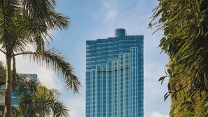 A tall, modern glass building surrounded by palm trees and greenery. - Kimpton Tsim Sha Tsui Hong Kong by IHG (Kowloon)