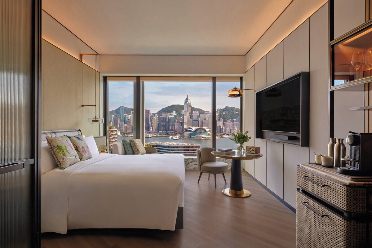 Ein modernes Hotelzimmer mit einem großen Bett, einem Essbereich, einem Fernseher und Blick auf die Stadt.