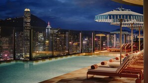 Une piscine sur le toit, dotée de chaises longues et offrant une vue sur le paysage urbain illuminé la nuit.