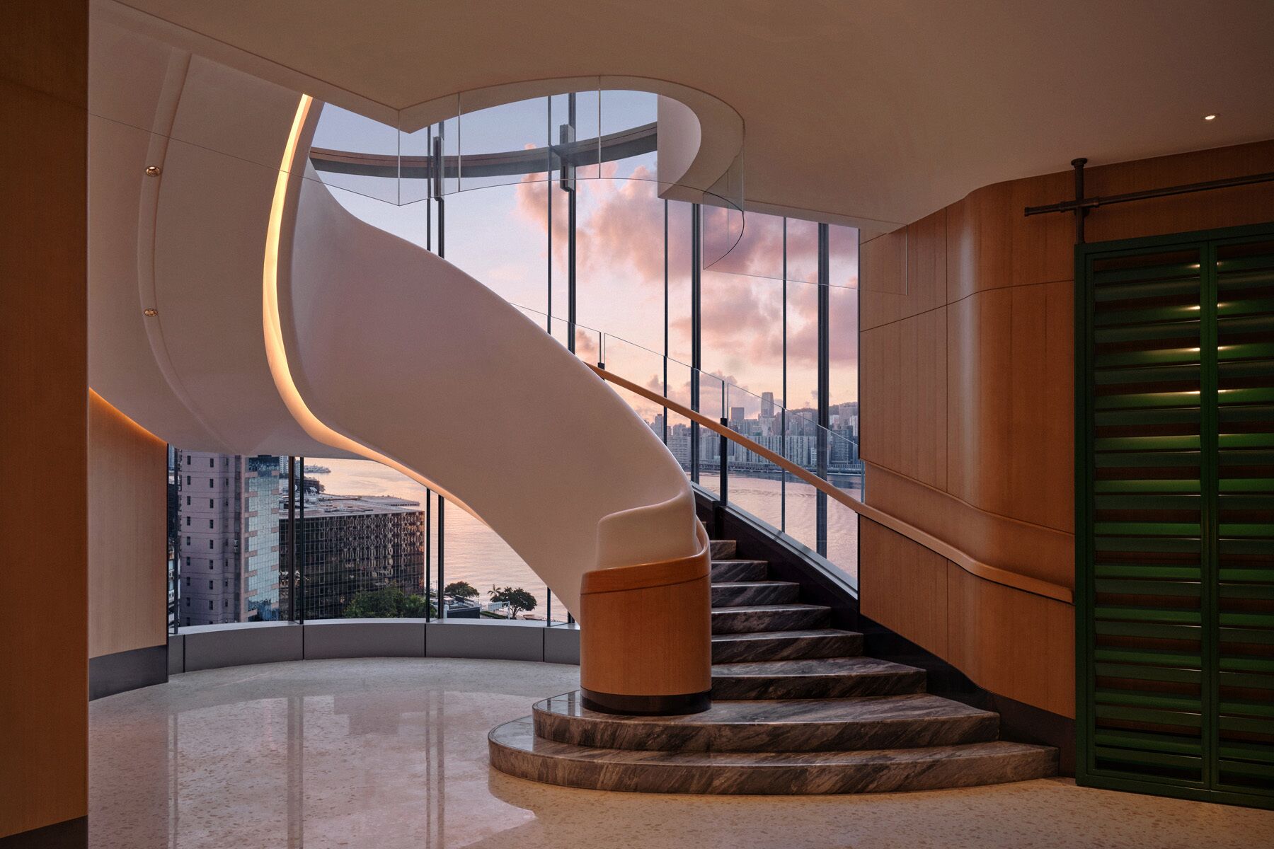A modern interior with a curved staircase, large windows, and a view of a cityscape.