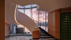 Un intérieur moderne avec un escalier en colimaçon, de grandes fenêtres et une vue sur le paysage urbain.