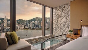 A modern hotel room with a large window offering a city view, a marble-tiled floor, a sofa, a bed, and a small side table with a lamp. - Kimpton Tsim Sha Tsui Hong Kong by IHG (Kowloon)