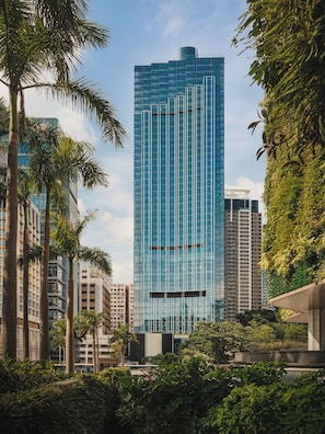 Un moderno edificio de gran altura con fachada de vidrio, rodeado de palmeras y otra vegetación.