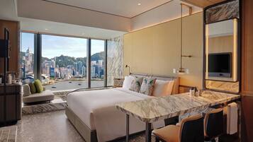A modern hotel room with a large bed, a dining table, and a city view.