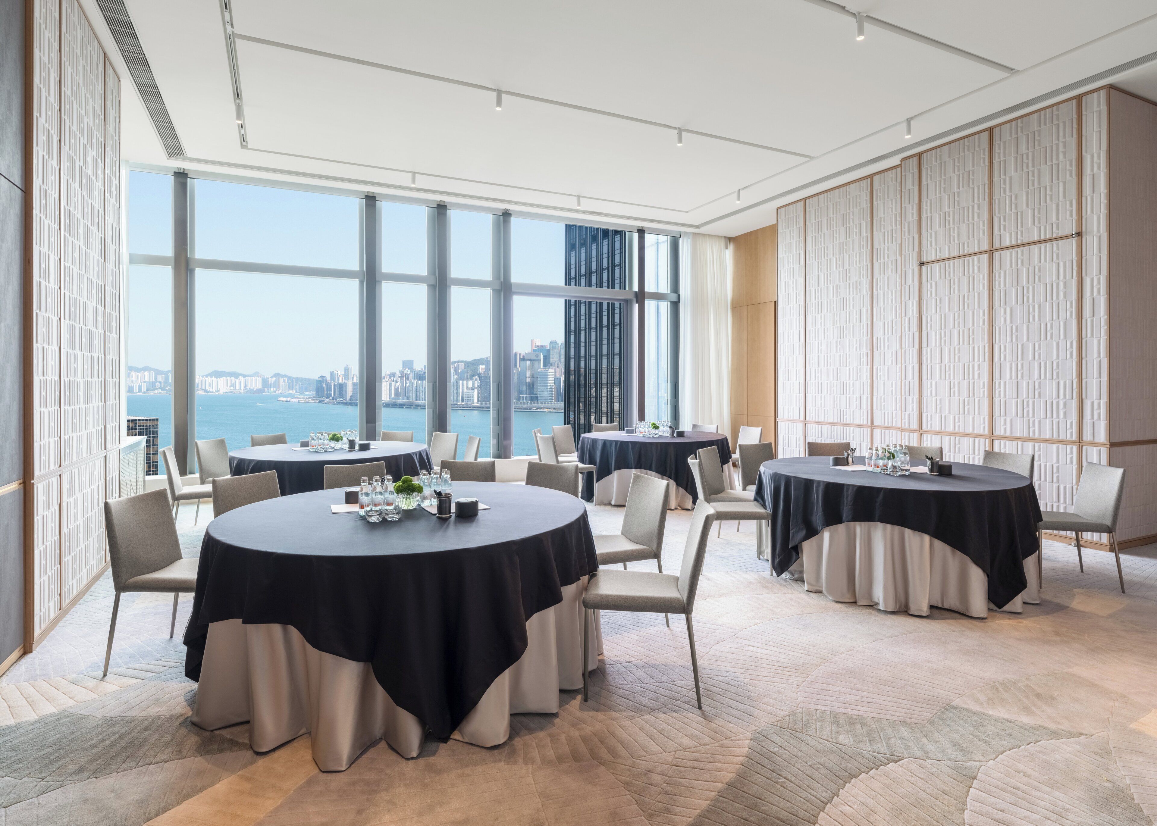 A modern conference room with round tables, chairs, and a large window offering a city view.