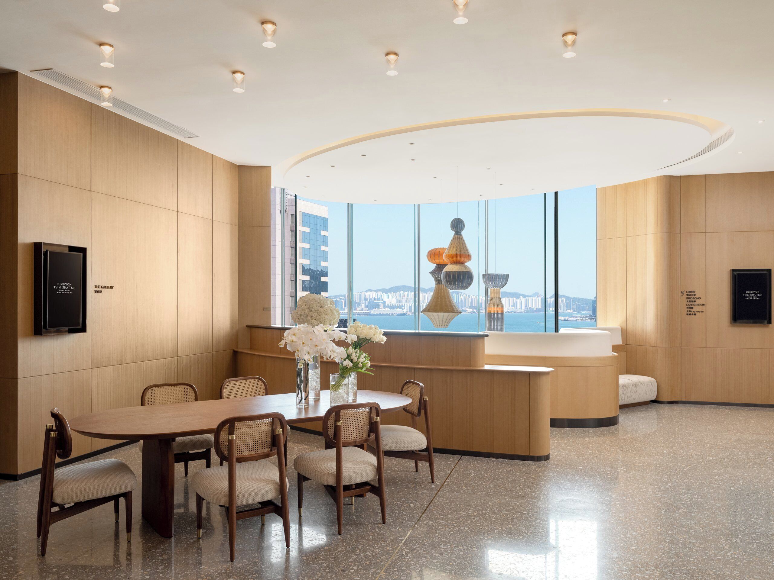 A modern hotel lobby with a round table, chairs, a reception desk, and a large window offering a city view.