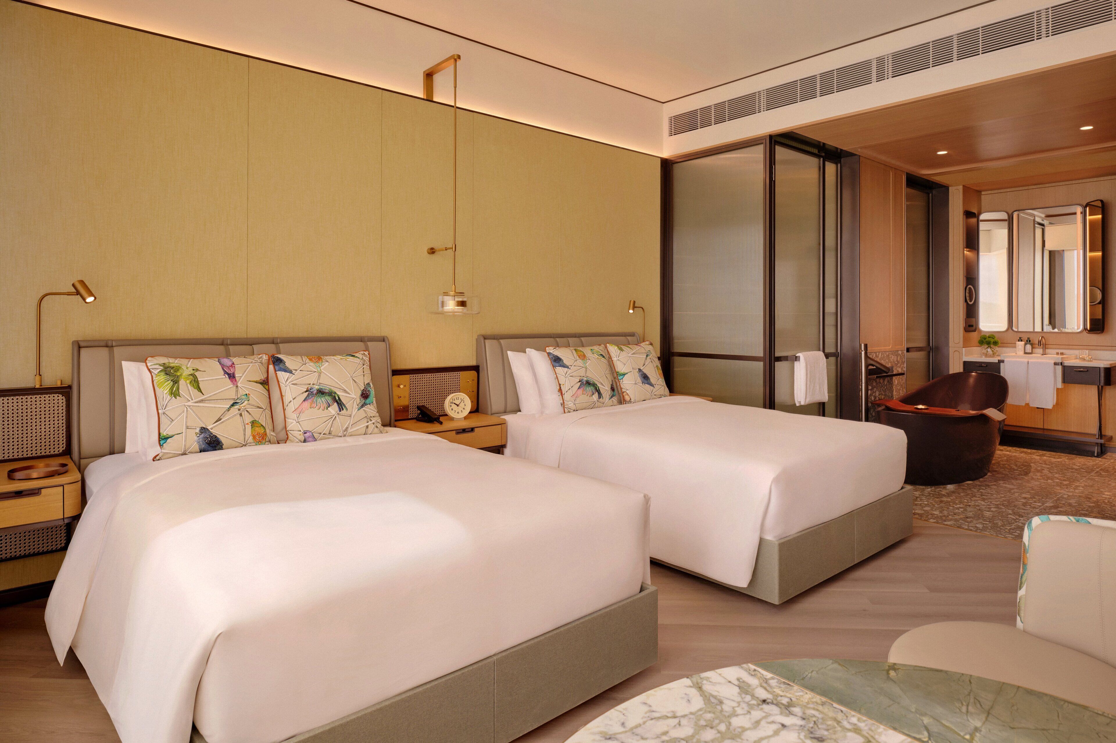 A hotel room with two beds, a sitting area, a large mirror, and a bathtub.
