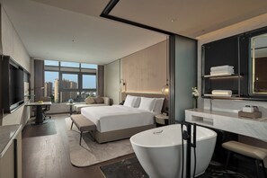 Une chambre d’hôtel moderne dotée d’un grand lit, d’un coin salon, d’une télévision et d’une salle de bain avec une grande baignoire.