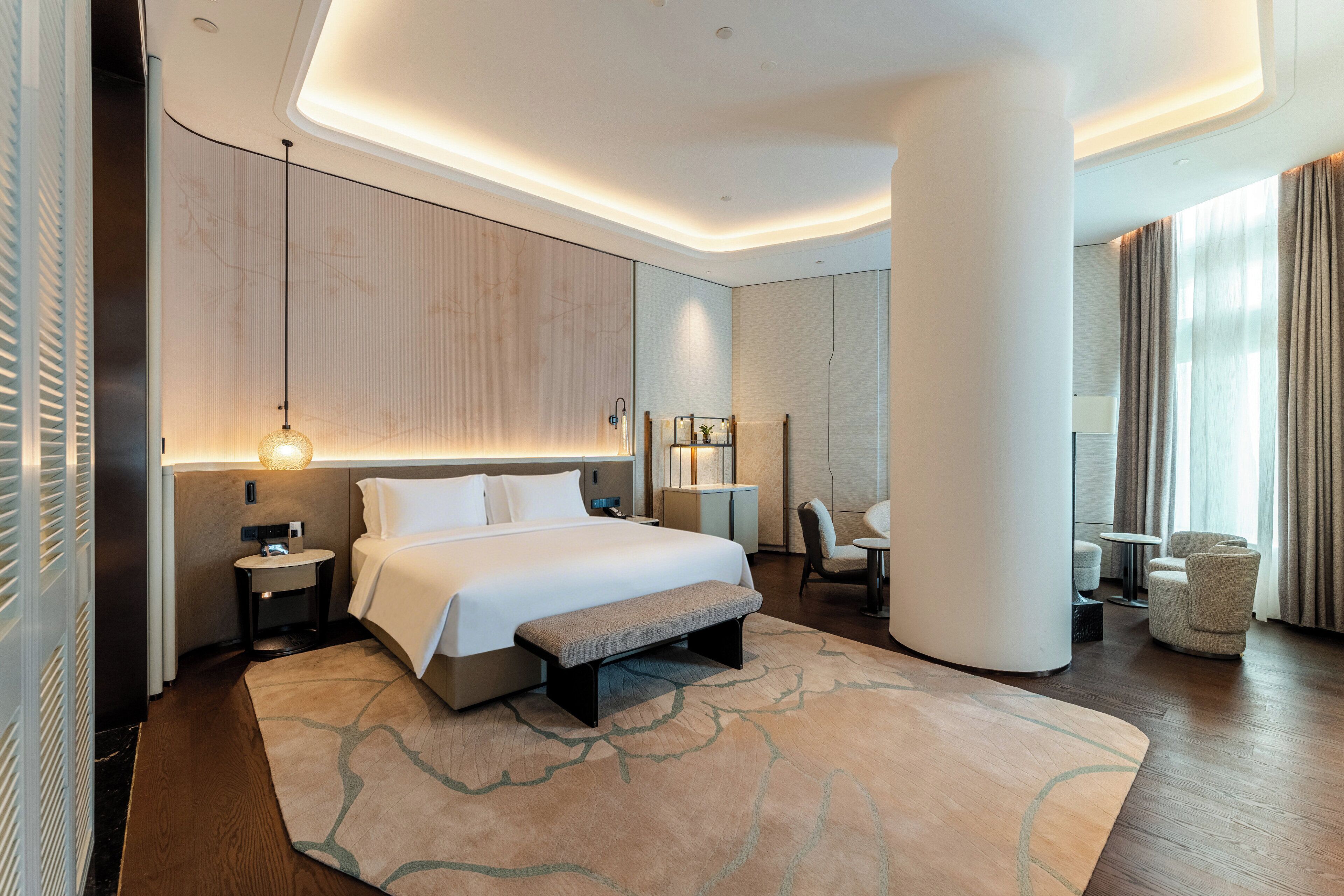 A modern hotel room with a large bed, a sitting area, and a view of the city.