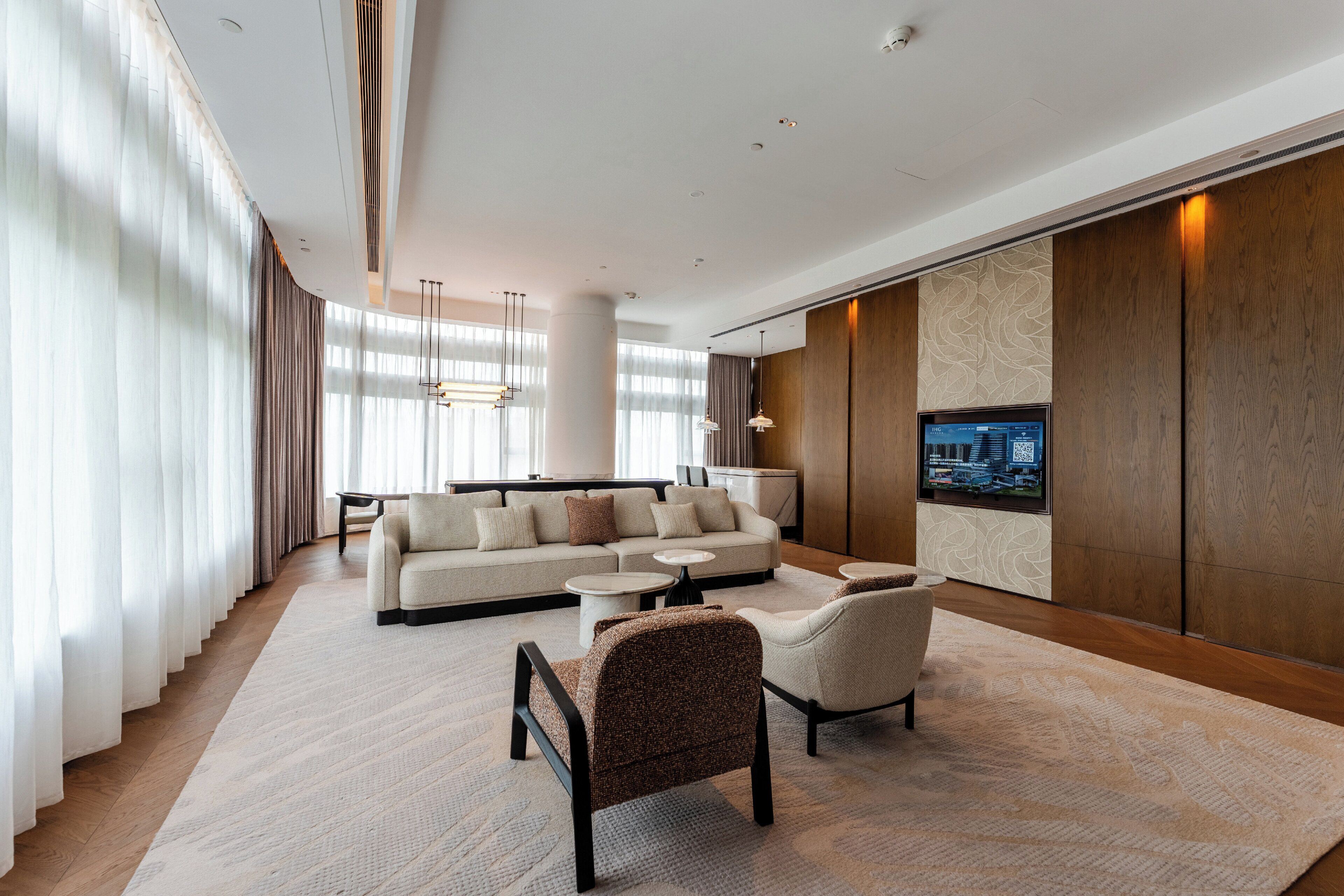 Habitación de hotel moderna con un sofá grande, dos sillones, una mesita de centro y un televisor de pantalla plana montado en la pared.