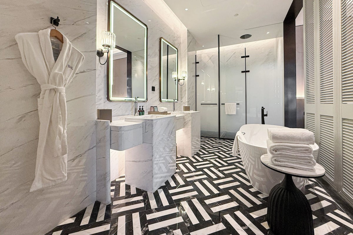 A modern bathroom with a marble vanity, large mirrors, a black and white patterned floor, and a glass-enclosed shower.