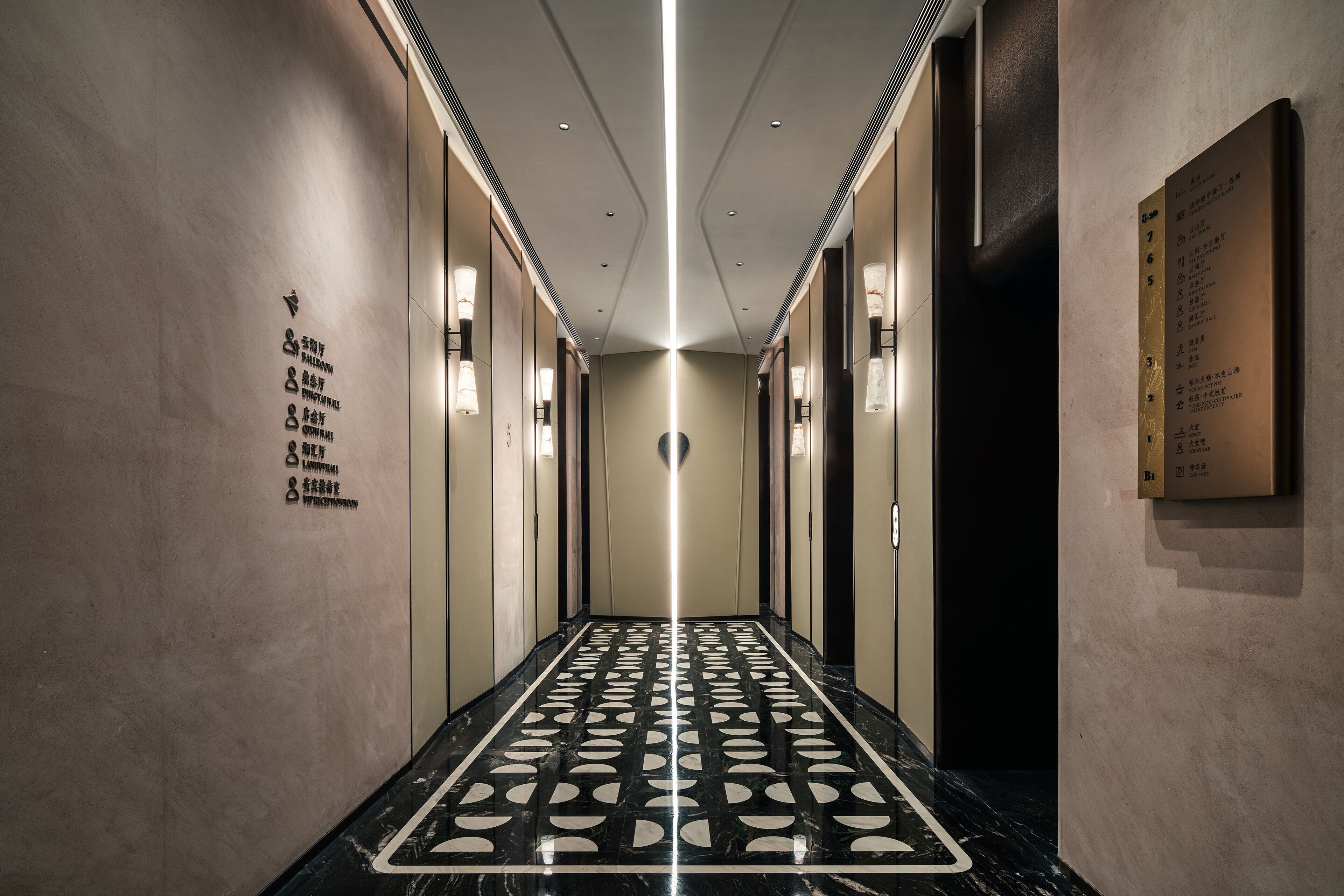 A hallway with a reflective floor, directional signs, and illuminated wall sconces.