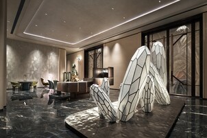 Un moderno vestíbulo de hotel con suelo de mármol, una recepción, zona de estar y grandes ventanales con vistas.
