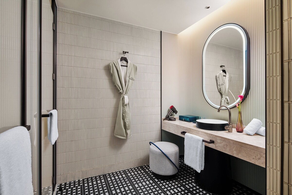 A modern bathroom with a tiled floor, a sink with a mirror, a towel rack, and a small trash bin.