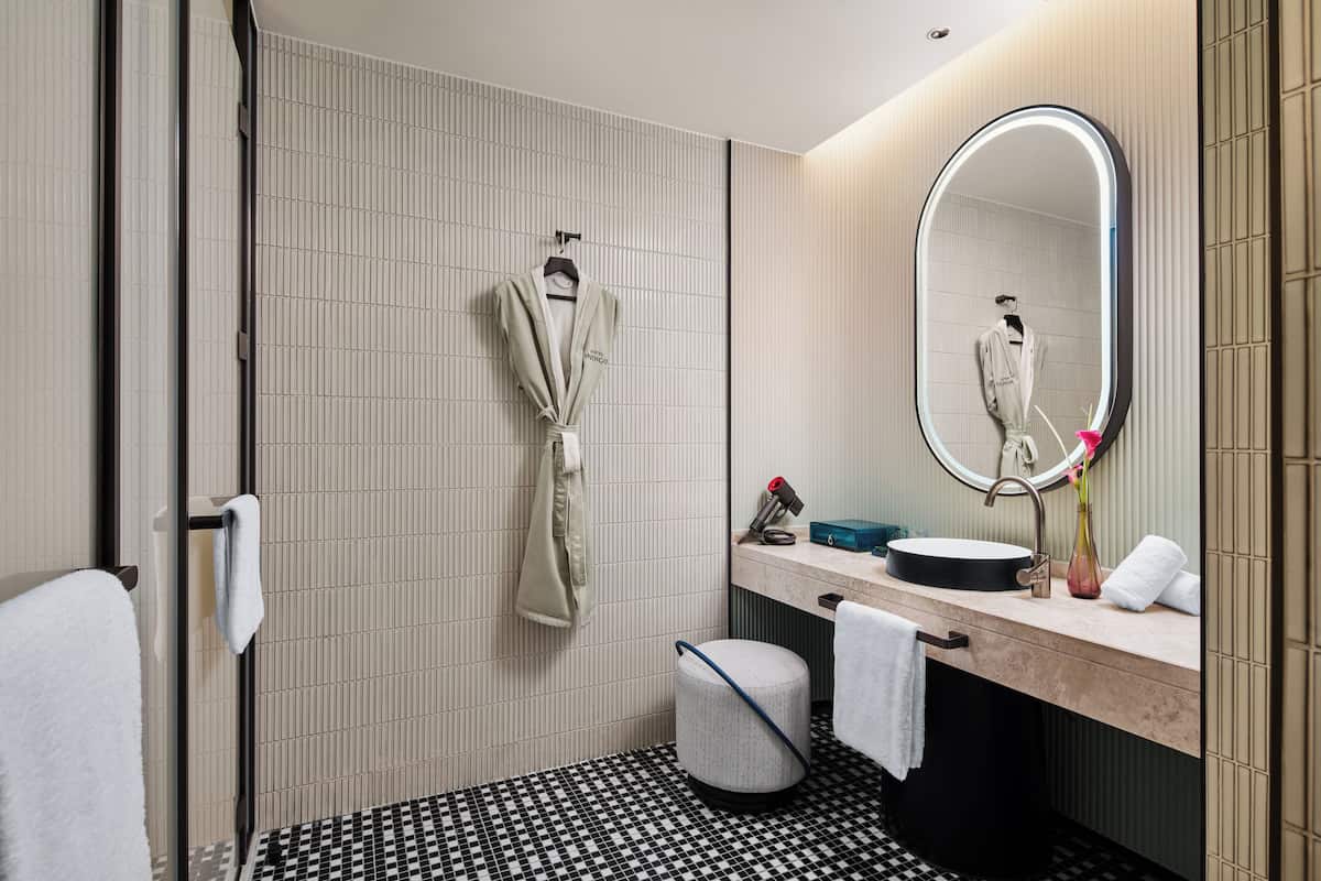 A modern bathroom with a tiled floor, a sink with a mirror, a towel rack, and a small trash bin.
