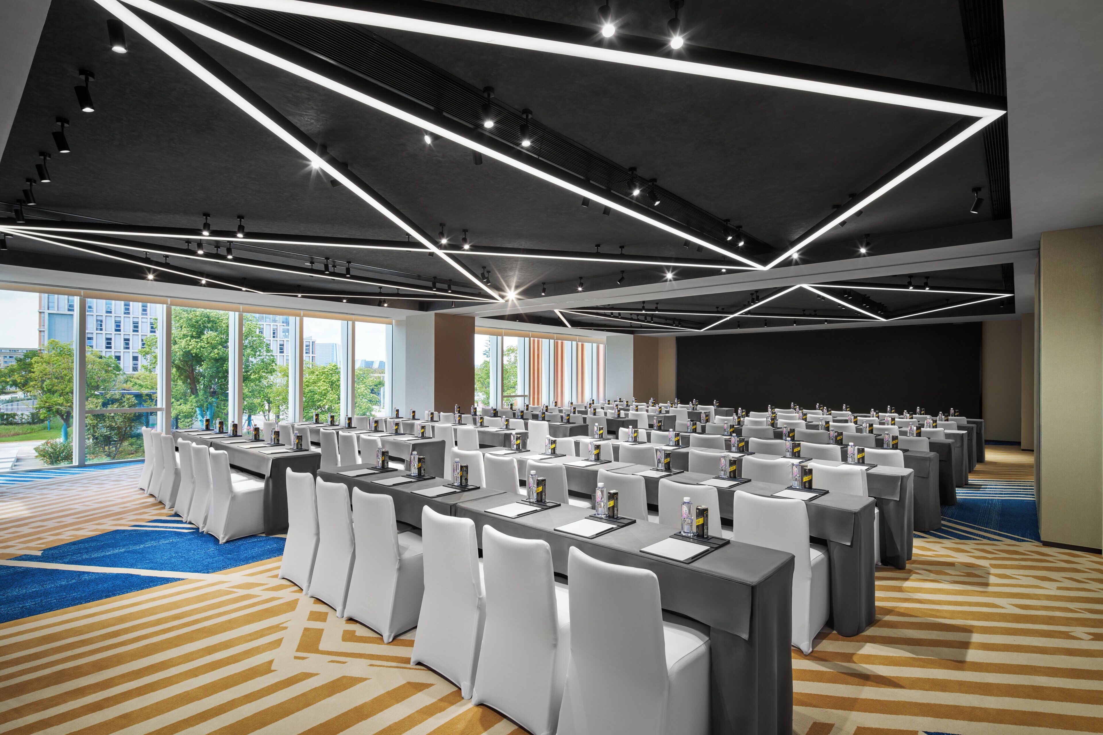Une salle de conférence avec des rangées de tables, des chaises blanches et un design moderne au niveau du plafond.