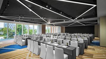 Une salle de conférence avec des rangées de tables, des chaises blanches et un design moderne au niveau du plafond.