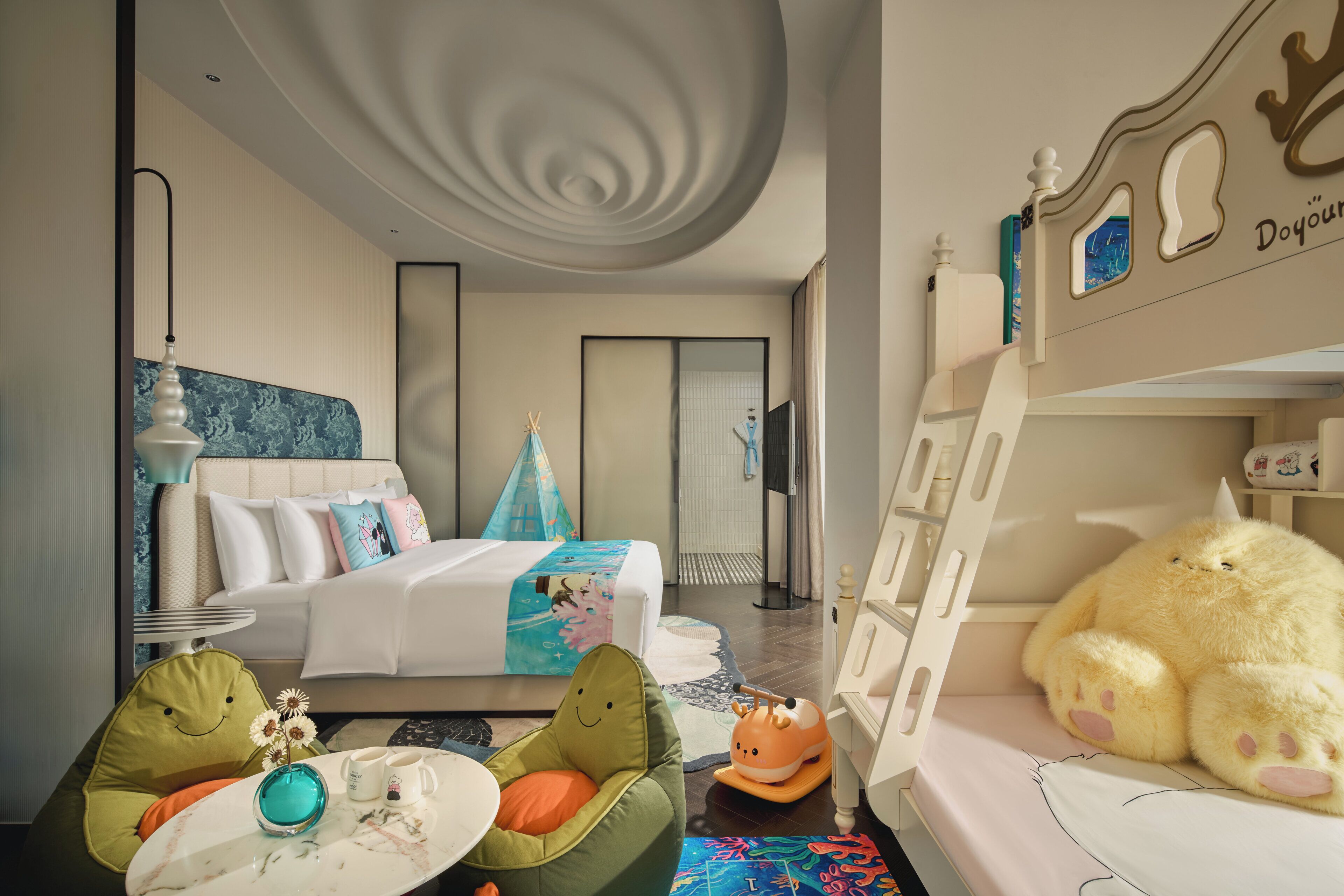 A hotel room with a bed, a bunk bed, a dining table, and a chair.