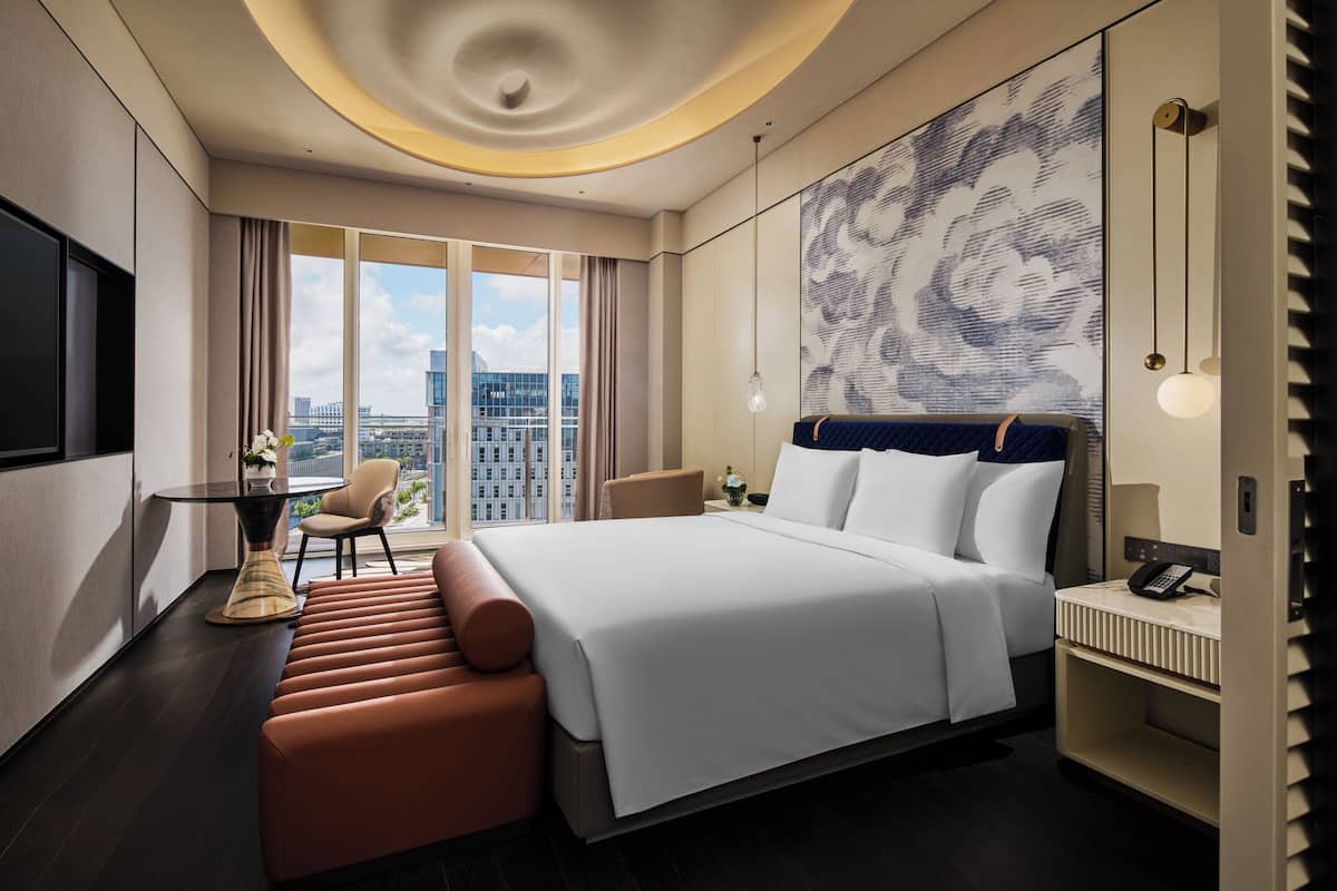 A modern hotel room with a large bed, a seating area, a desk, and a city view.