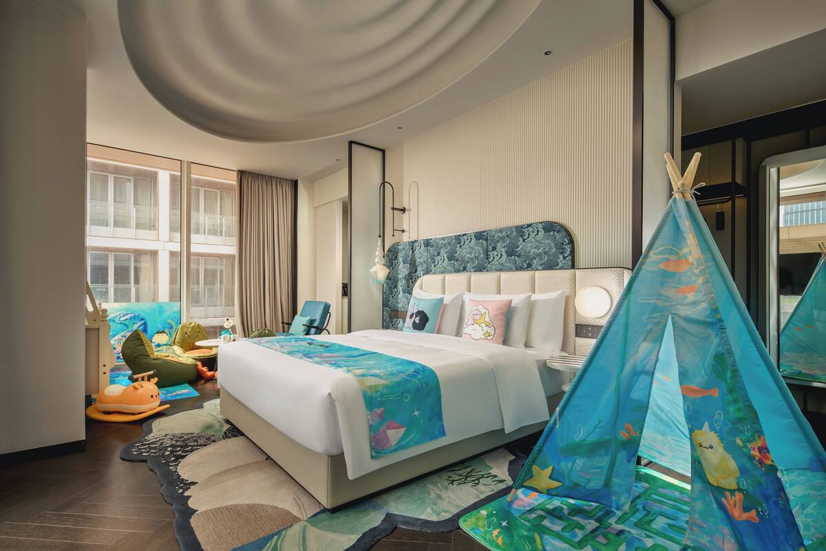 A hotel room with a bed, a window, a chair, and a tent-like structure.
