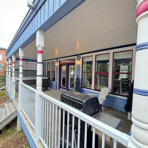 A covered outdoor deck with a grill and seating area, columns with decorative caps, and a view of the surrounding area.