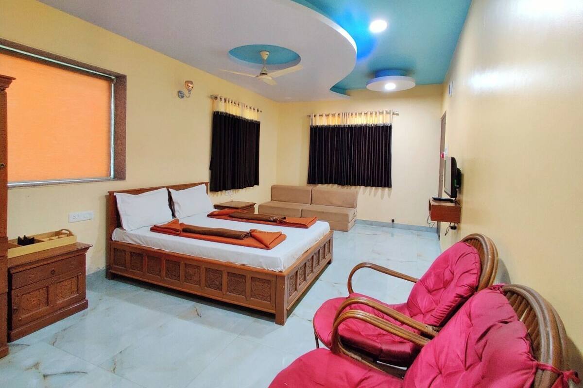 A bedroom with a bed, a sofa, a chair, a TV, and a ceiling fan.