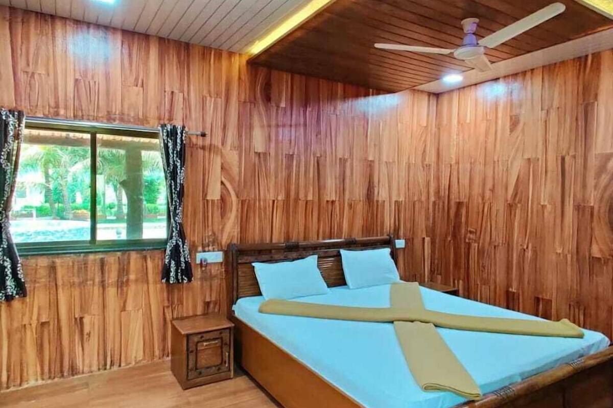 A wooden-paneled bedroom with a bed, nightstand, and window with curtains.