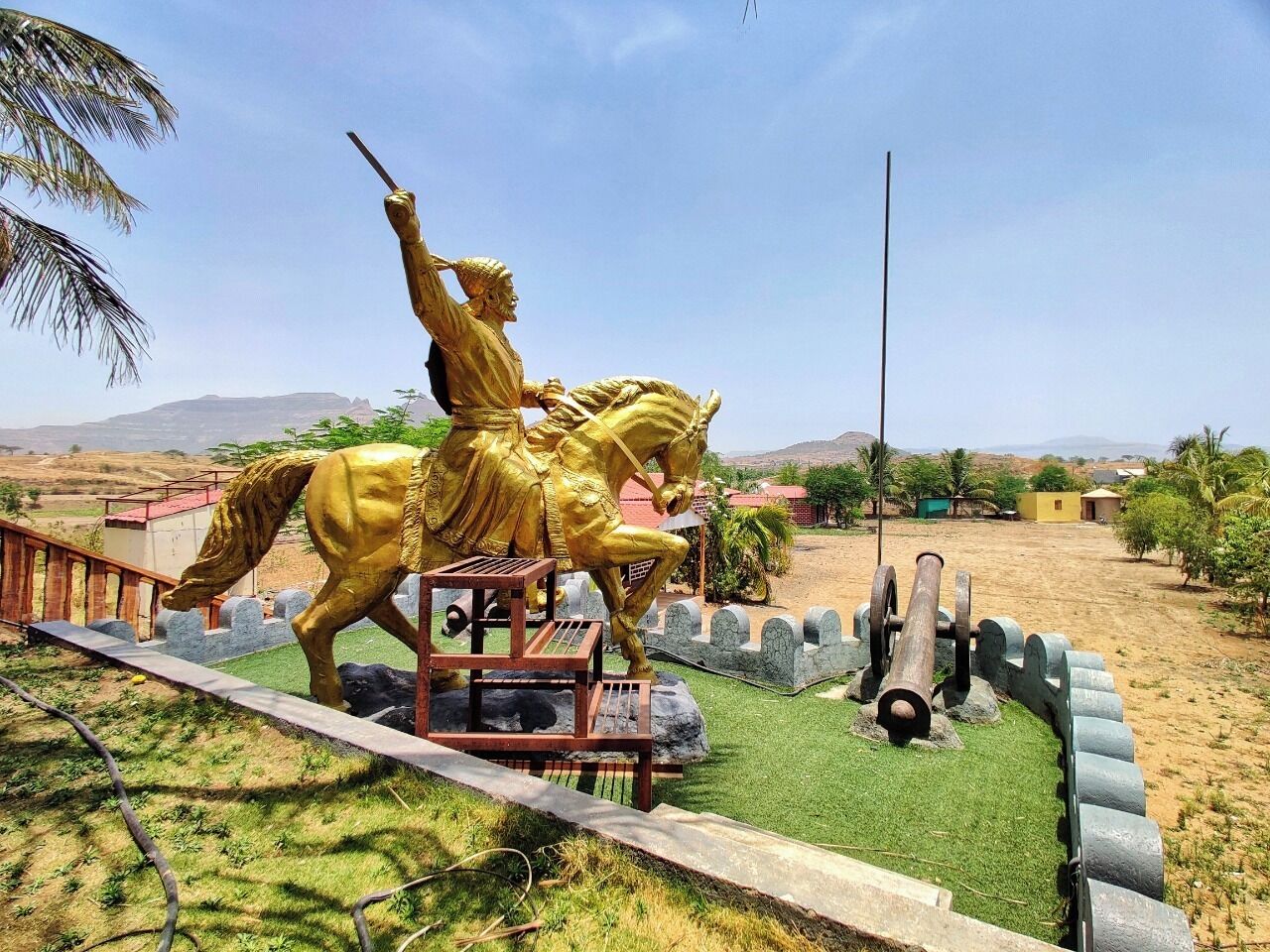Estàtua daurada d'una figura a cavall, un cañón i un mur de pedra en una zona enjardinada.