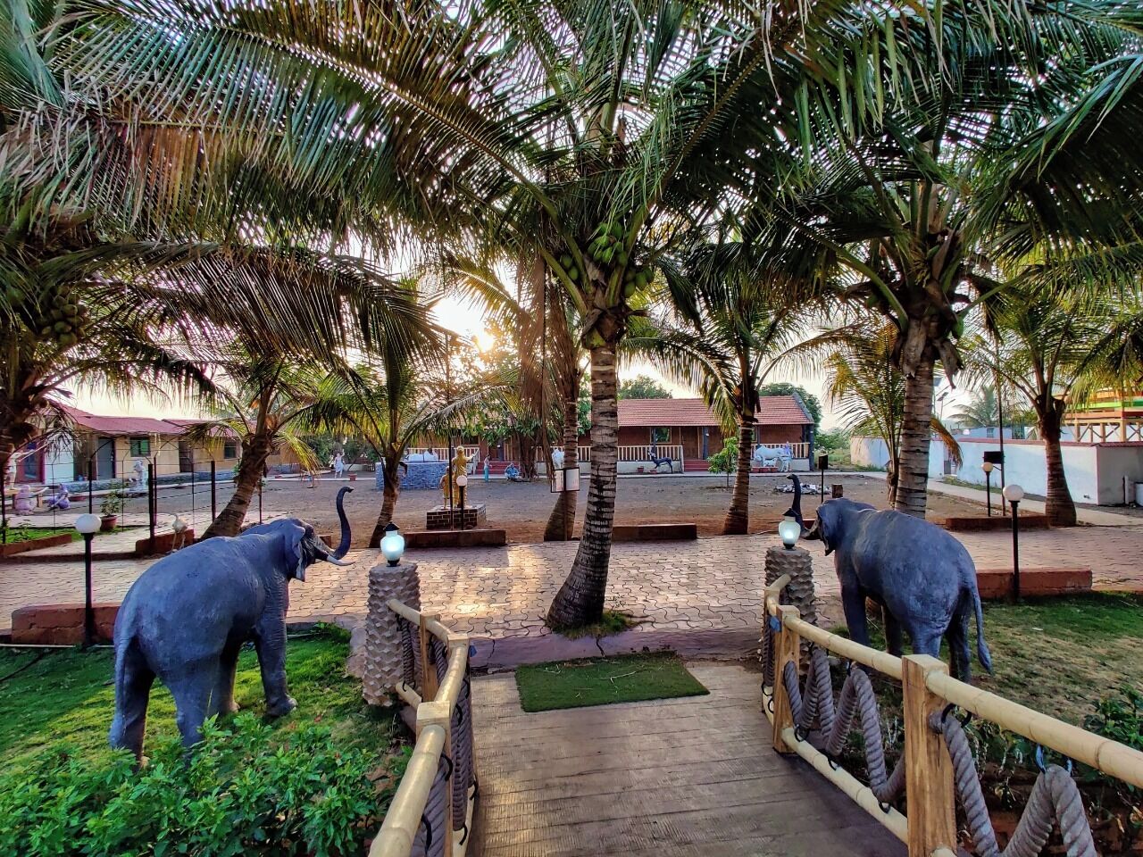 A pathway with two elephant statues, palm trees, and a brick-paved area.