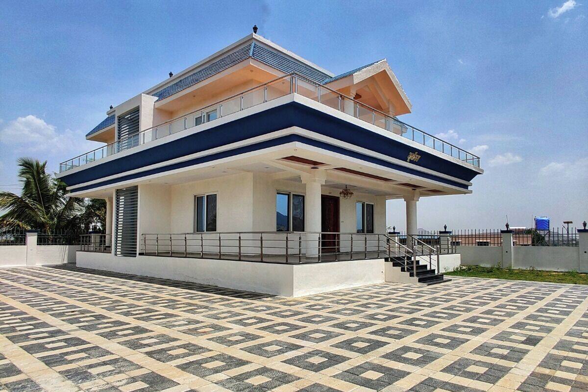 A modern two-story house with a balcony, a tiled patio, and a clear sky.