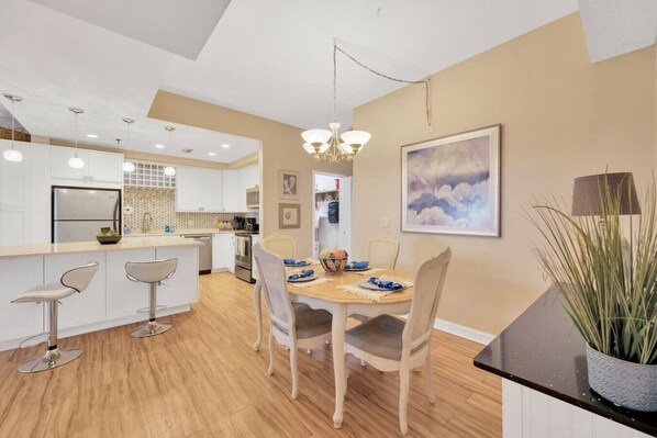A modern kitchen with white cabinets, a central island with bar stools, and a dining area with a wooden table and chairs.