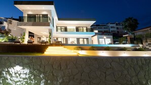 A modern multi-story house with a prominent staircase leading to the entrance, surrounded by a stone wall and a well-lit pool area. - Beachfront Villa Nautilux with Pool (Seget Donji)