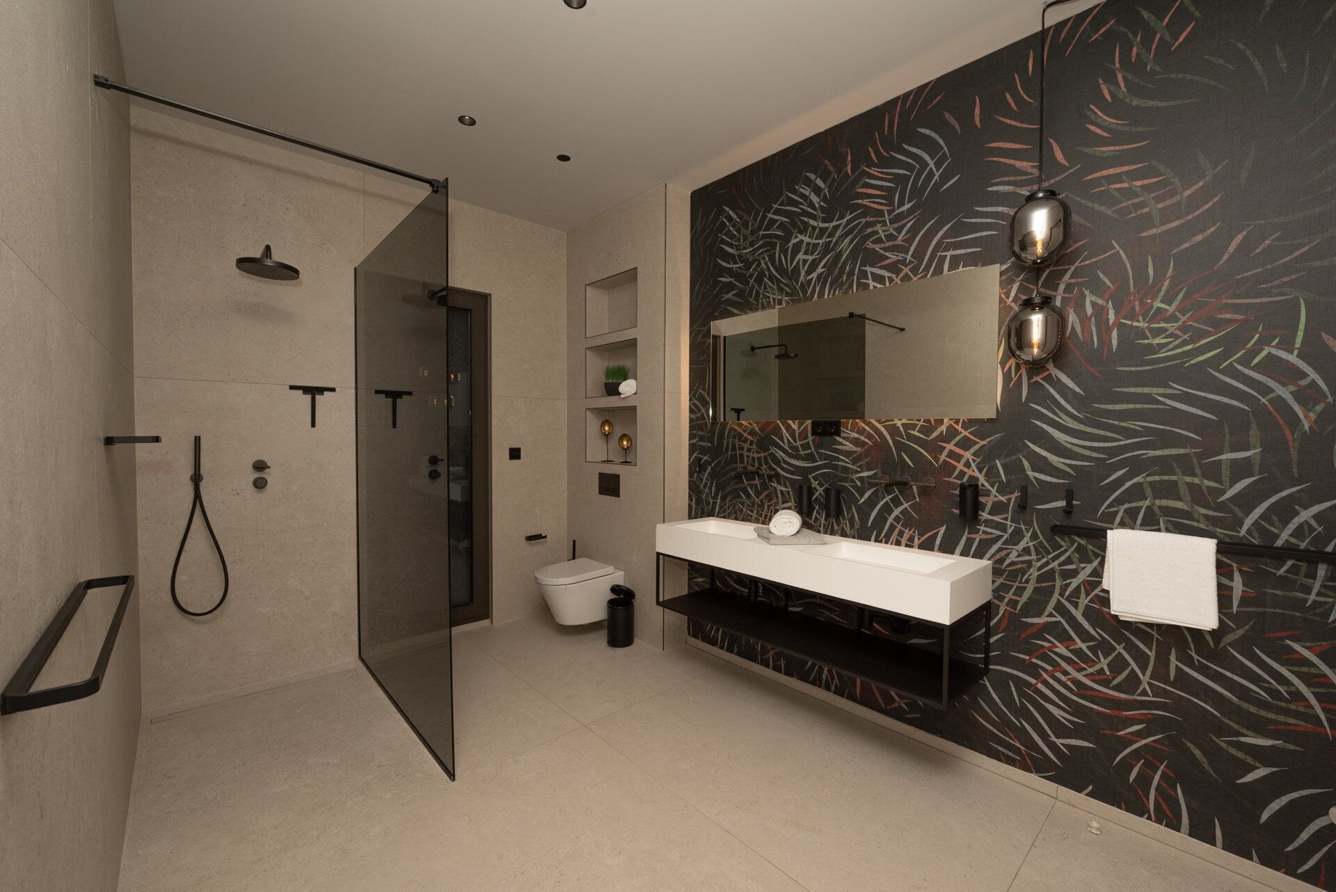 A modern bathroom with a glass shower enclosure, a white sink with a mirror, and a decorative wall with a leaf pattern.