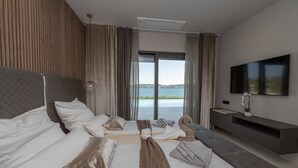 A modern hotel room with a large bed, a sofa, a TV, and a view of the sea. - Beachfront Villa Nautilux with Pool (Seget Donji)