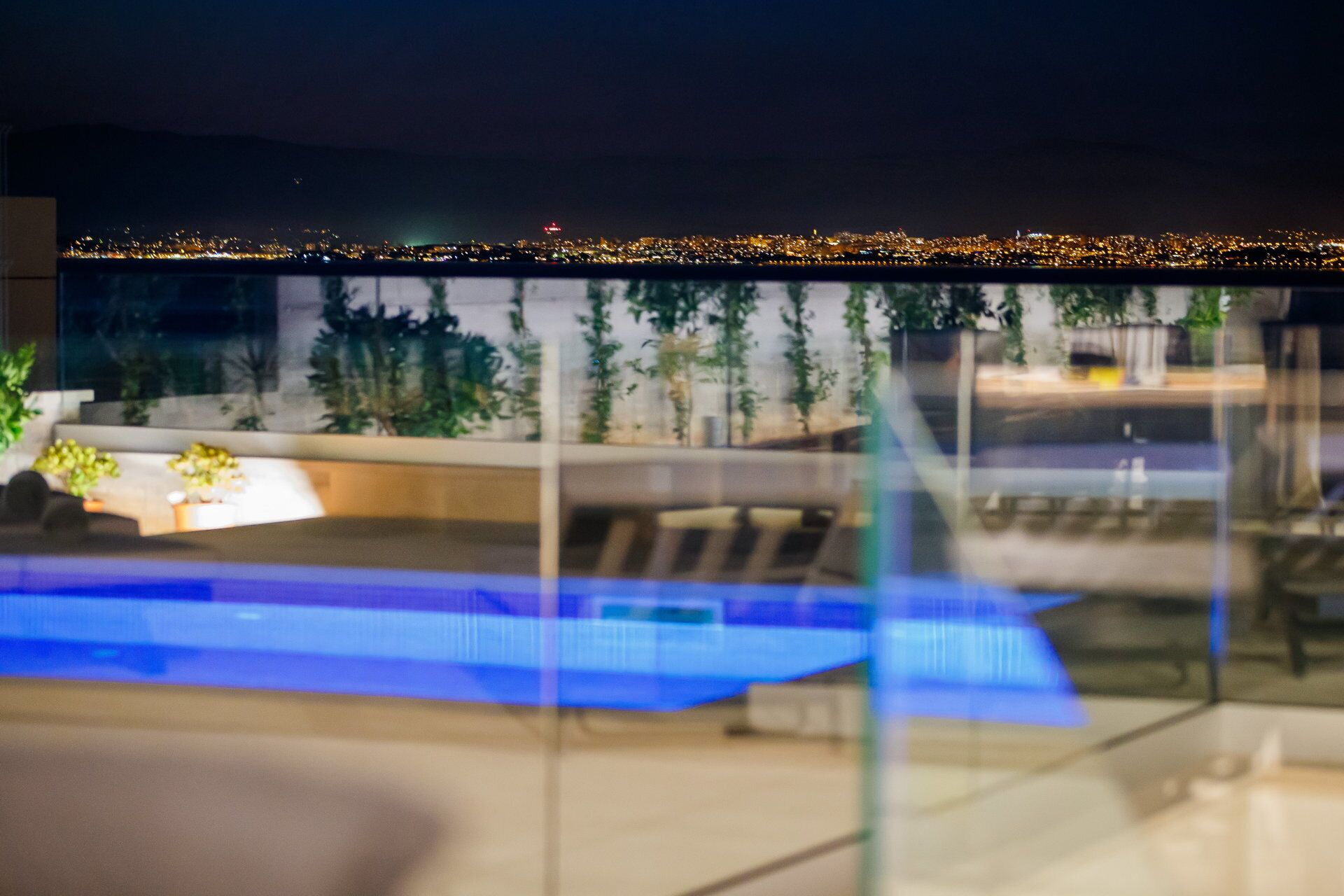 Ein modernes Gebäude mit Glasfassade, Poolbereich und Blick auf eine nächtliche Skyline.