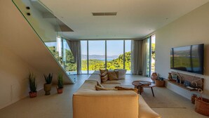 Una sala de estar moderna con un sofá grande, un televisor y vistas a un paisaje montañoso a través de amplios ventanales.