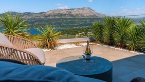 Una terraza con una mesa, una botella de vino y vistas a un paisaje montañoso.