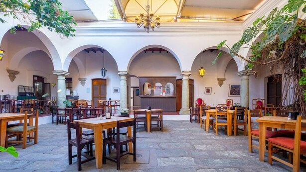 An indoor dining area with multiple wooden tables and chairs, stone flooring, and arches.