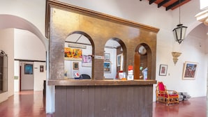 A reception desk with a clock, framed artwork, and a chair in a spacious lobby with tiled flooring and arched ceilings.
