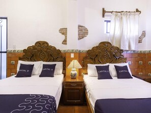 A hotel room with two beds, each with a headboard, a nightstand, and a lamp.