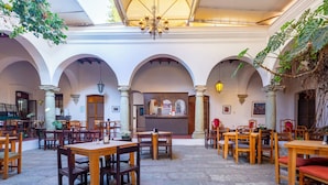 A spacious courtyard with stone flooring, wooden tables and chairs, and a central bar area.