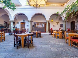 Ein geräumiger Innenhof mit Steinböden, Holztischen und -stühlen sowie einer Bar in der Mitte.