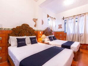 Habitación de hotel con dos camas, cabecero de madera, una lámpara y una ventana con cortinas.