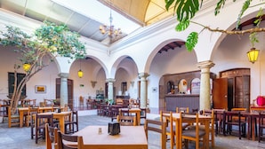 A spacious indoor courtyard with multiple wooden tables and chairs, stone flooring, and a central bar area.